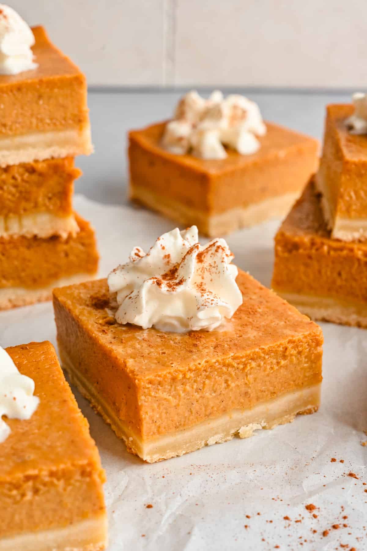 Pumpkin pie bars on a piece of white parchment paper and dusted with cinnamon.