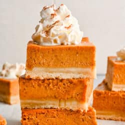 Three pumpkin pie bars stacked on top of each other with whipped cream on top.