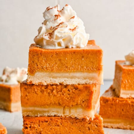 Three pumpkin pie bars stacked on top of each other with whipped cream on top.