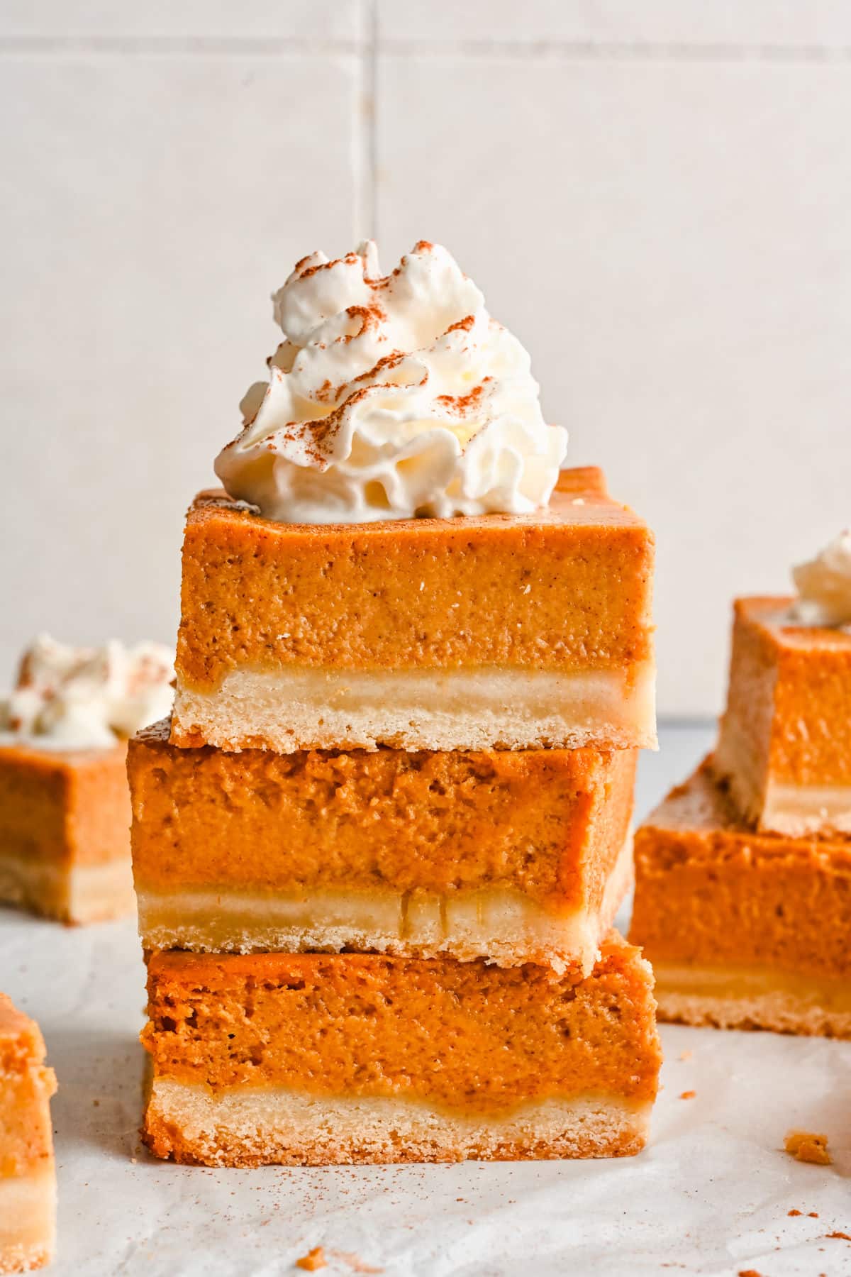 Three pumpkin pie bars stacked on top of each other with whipped cream on top.