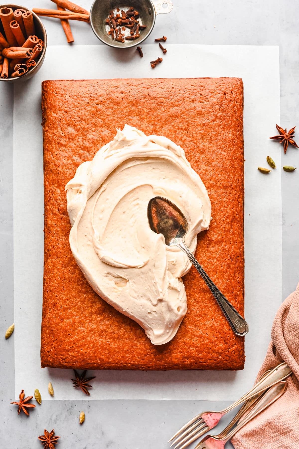 A vintage silver spoon spreading cream cheese frosting onto a spice cake.