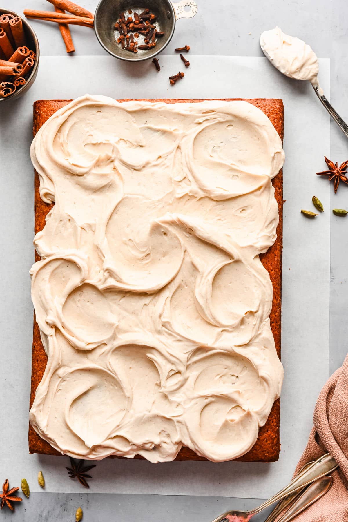 A frosted spice cake with a spoon full of cream cheese frosting next to it.