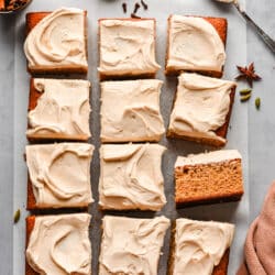 A pumpkin spice cake frosted with cream cheese frosting and surrounded by cinnamon sticks and spices.