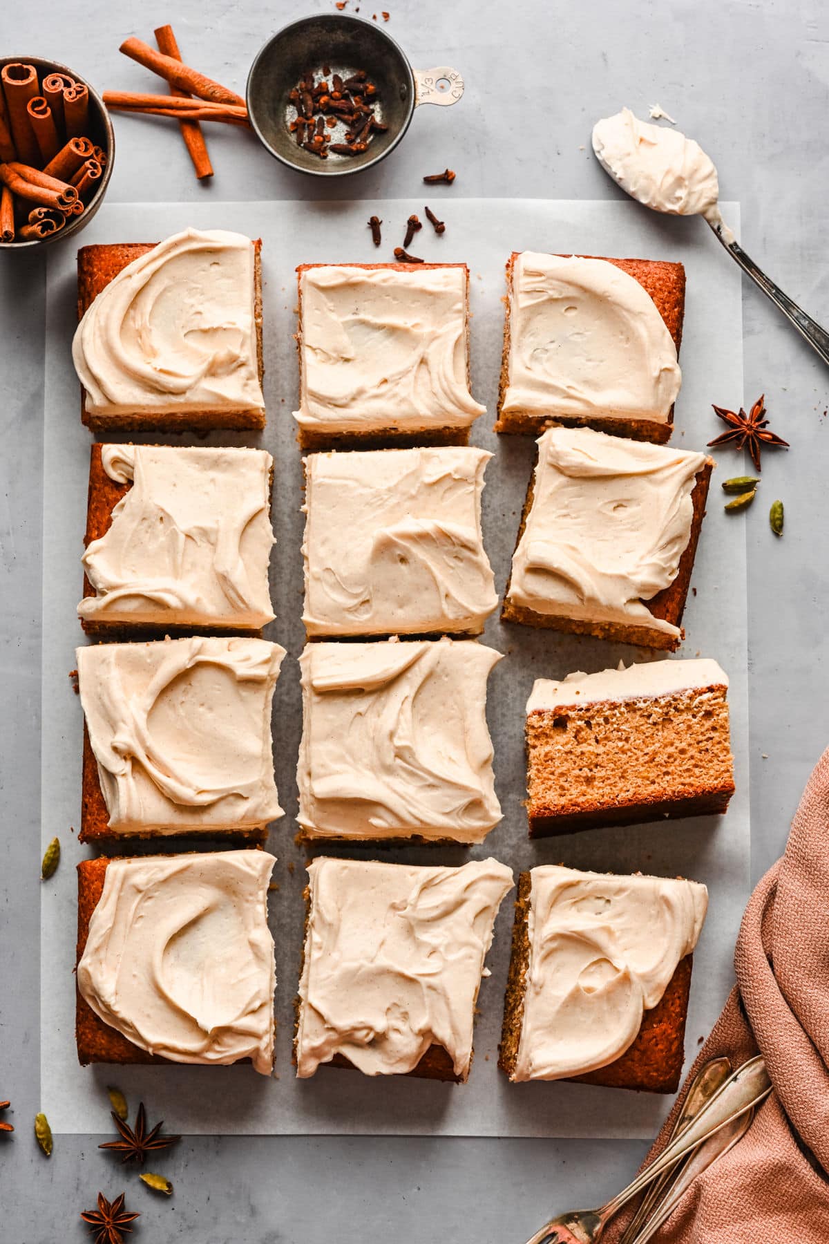 A pumpkin spice cake frosted with cream cheese frosting and surrounded by cinnamon sticks and spices.