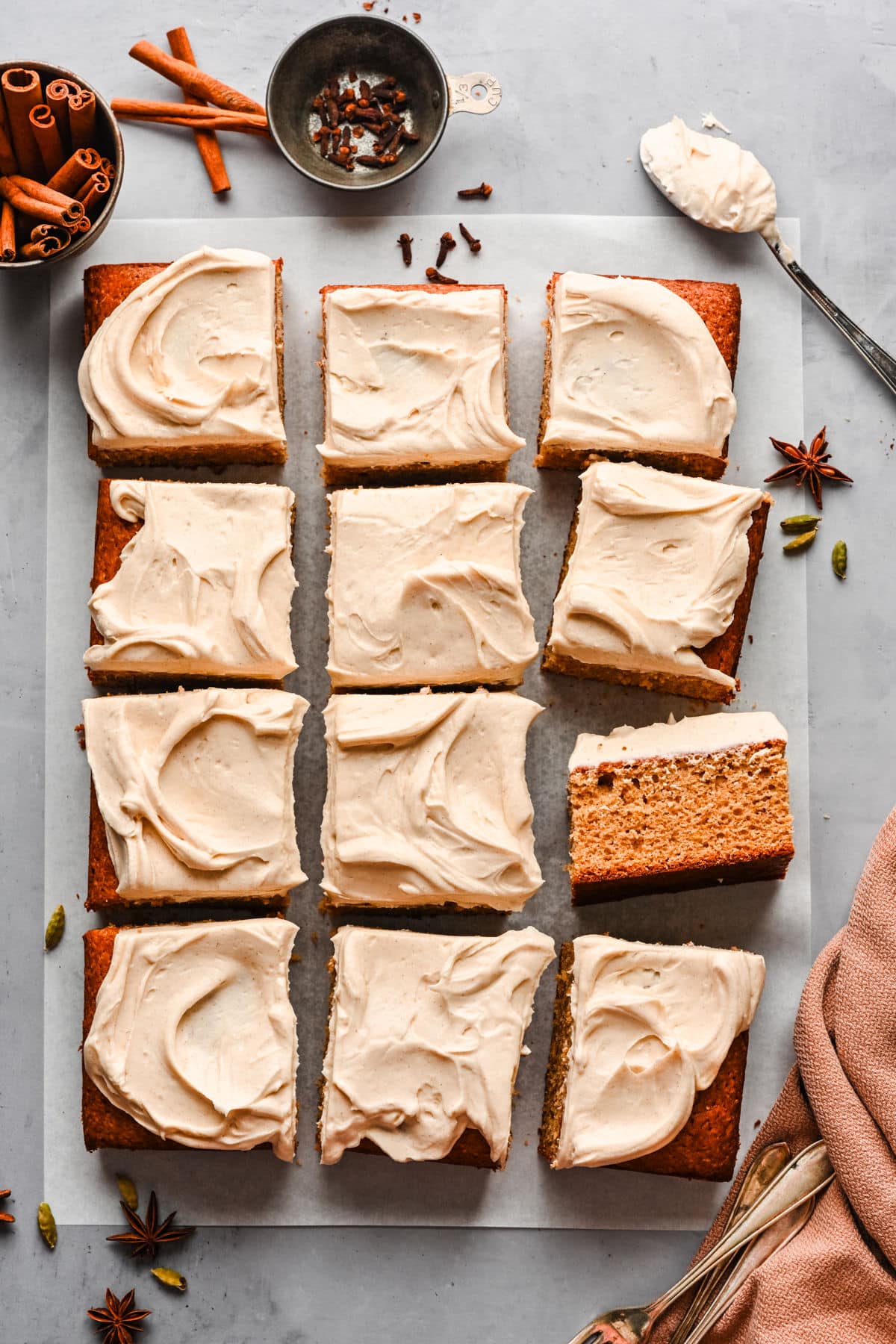 A pumpkin spice cake frosted with cream cheese frosting and surrounded by cinnamon sticks and spices. 