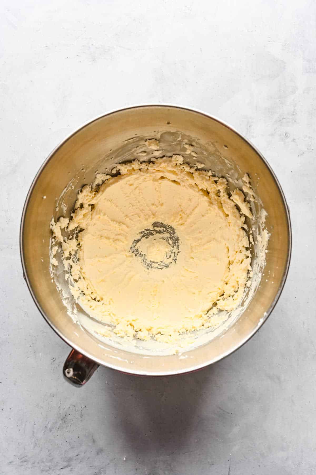 Beaten butter and cream cheese in a silver mixing bowl. 