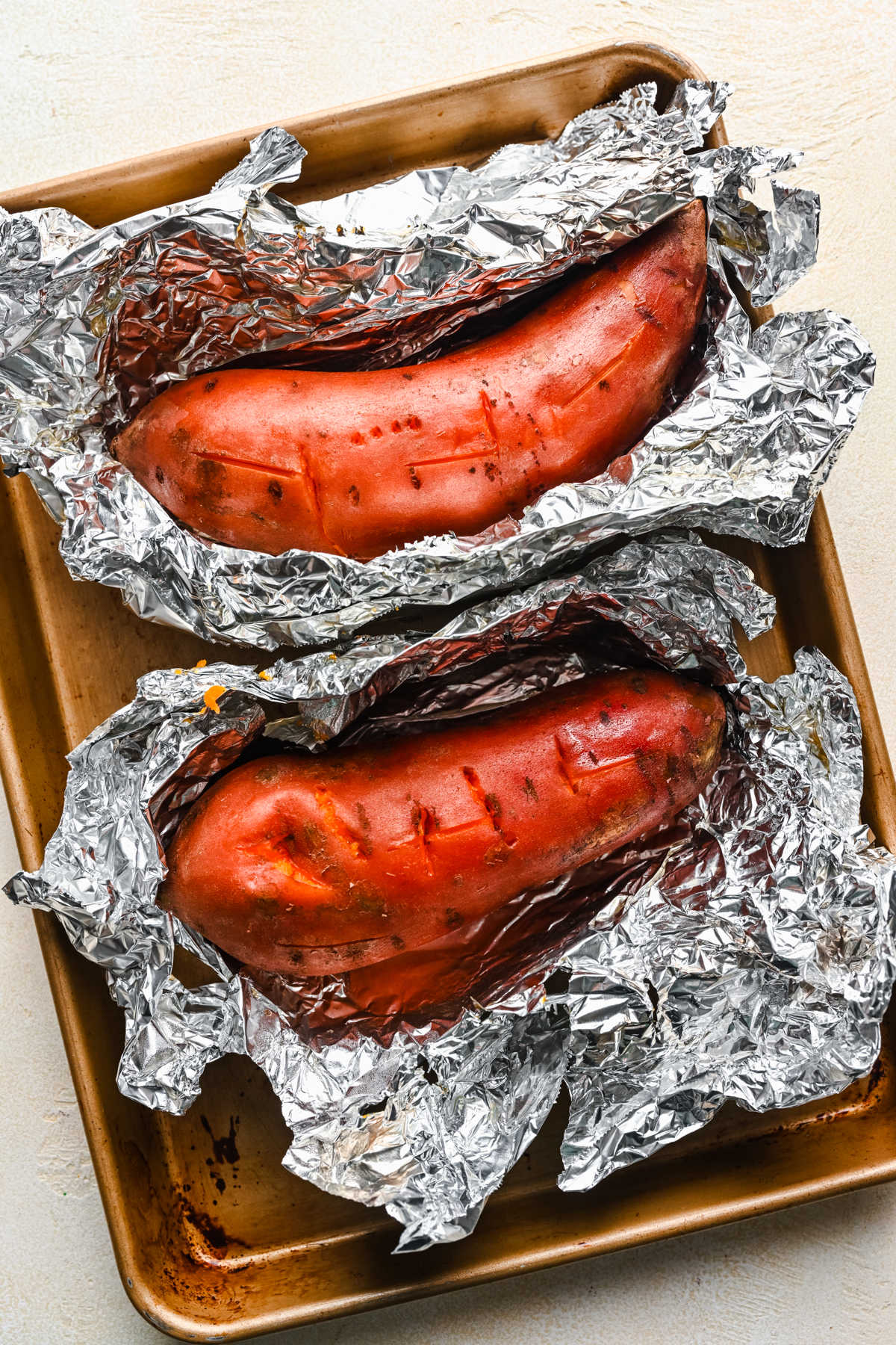 Sweet potatoes in pieces of open foil on a baking sheet. 