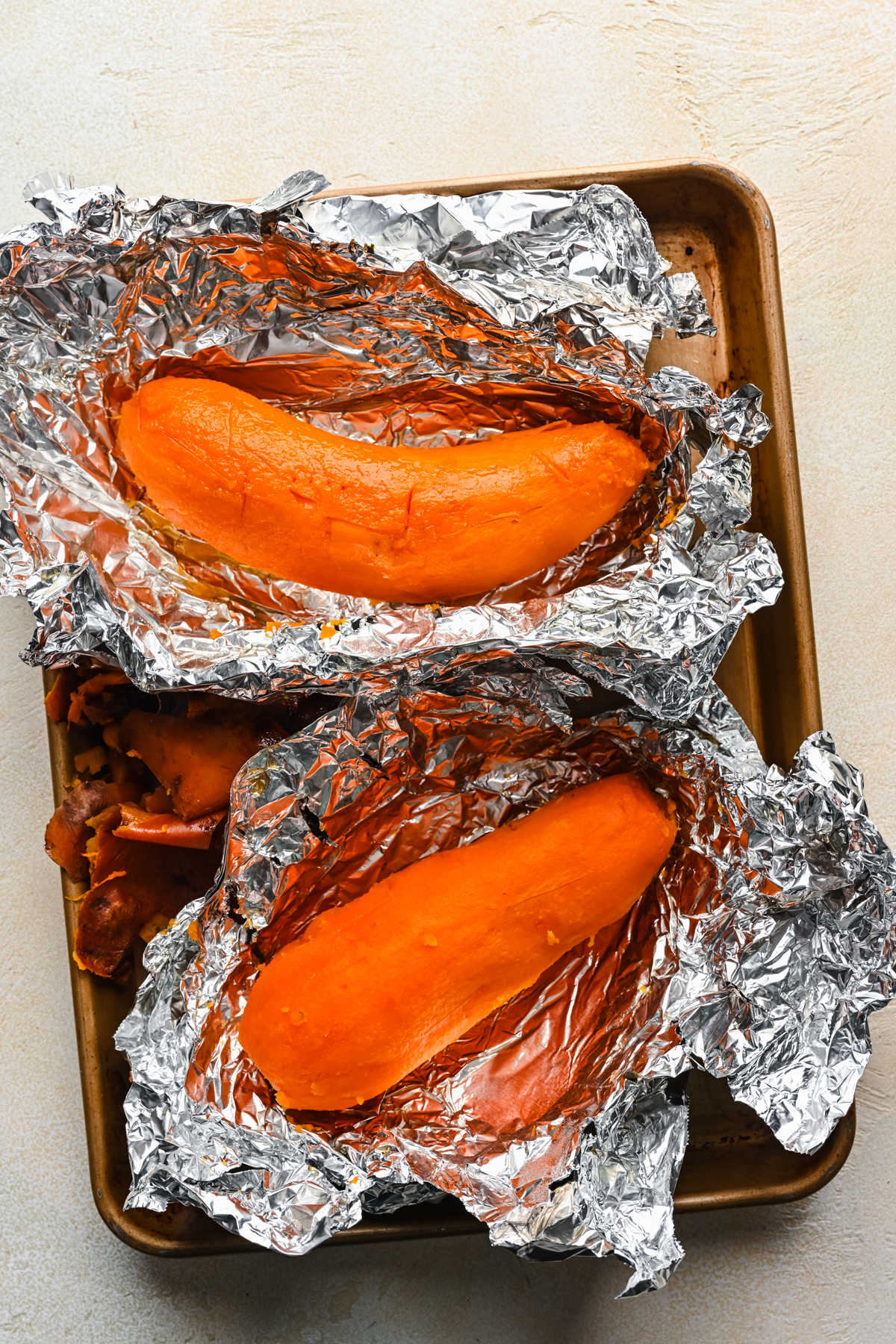 Sweet potatoes with no skin in aluminum foil on a baking sheet. 
