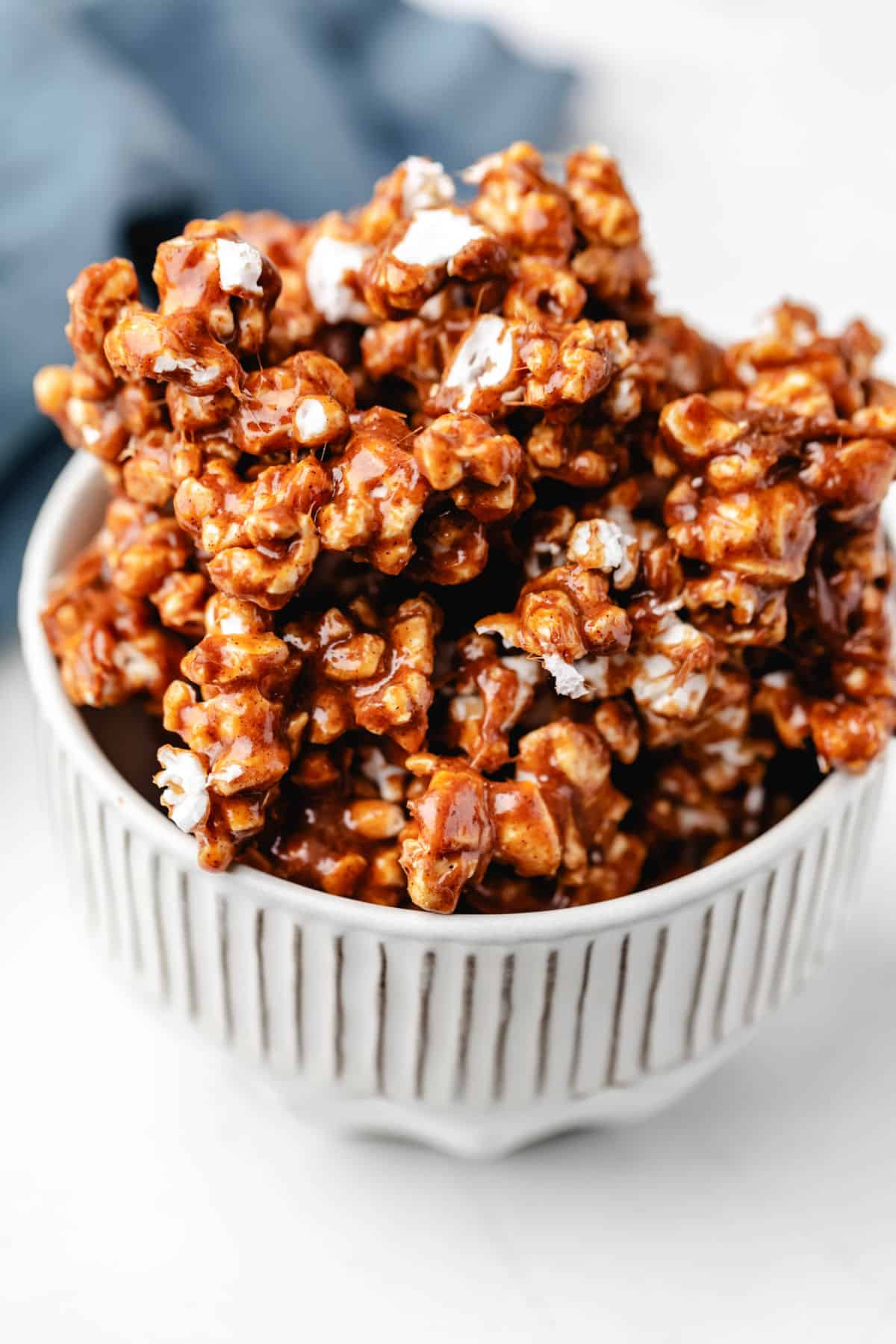 Cinnamon Bun Popcorn Cinnamon bun popcorn in a white dish next to a blue kitchen linen.