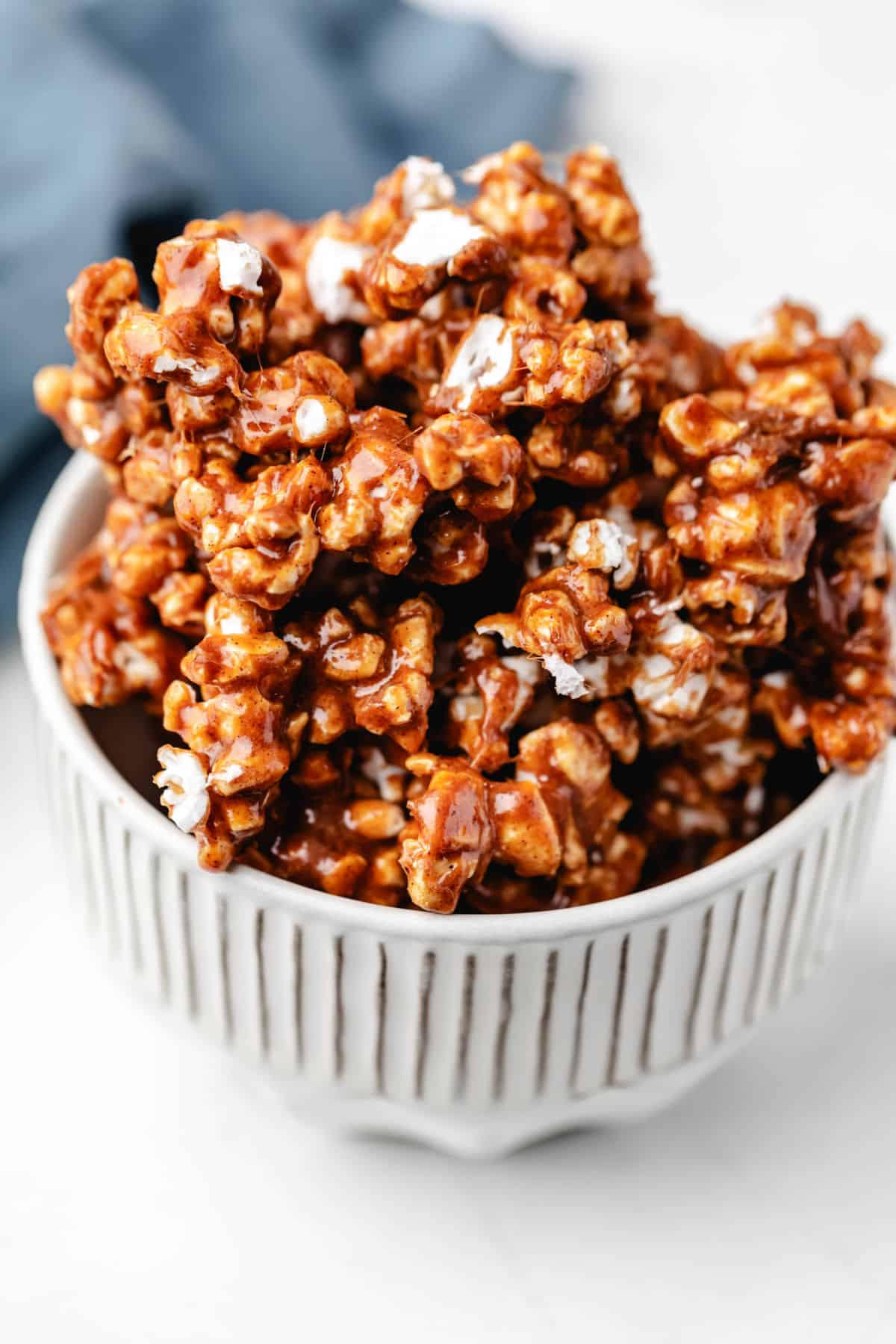 Cinnamon bun popcorn in a white dish next to a blue kitchen linen.