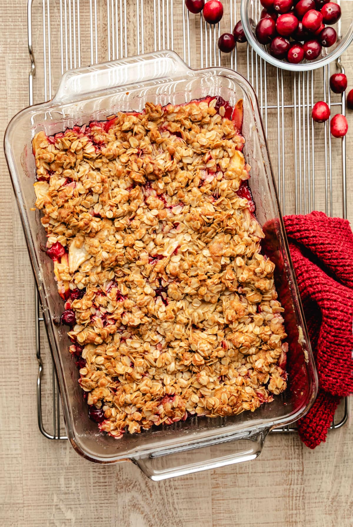 A glass dish of cranberry apple crisp at an angle on a wire cooling rack.