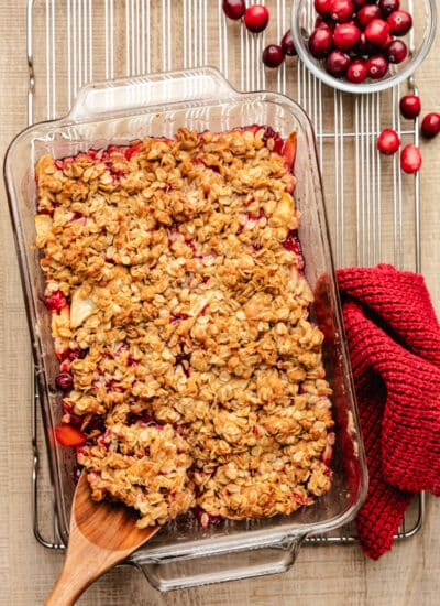 A wooden spoon scooping out cranberry apple crisp from the dish.