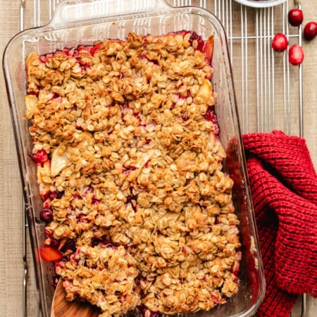 A wooden spoon scooping out cranberry apple crisp from the dish.