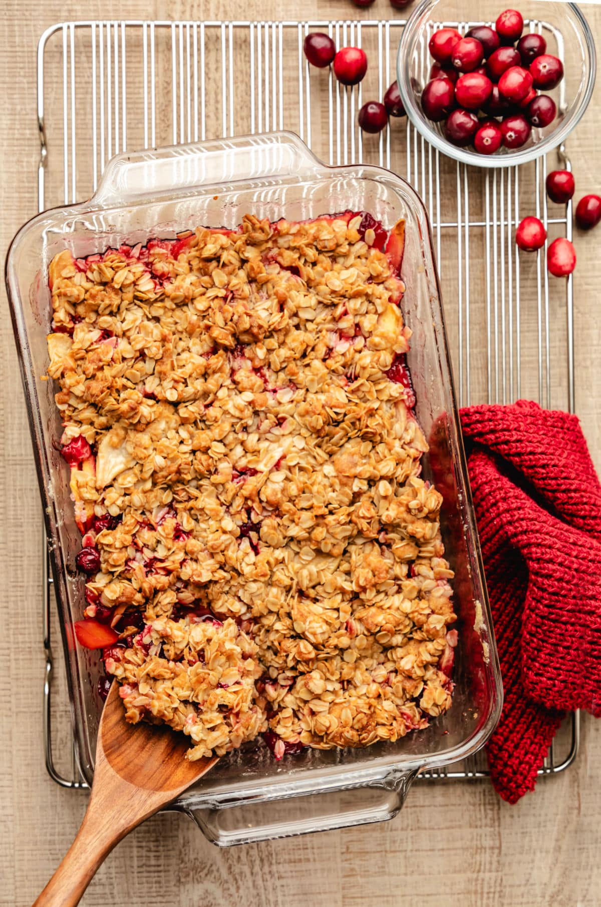 A wooden spoon scooping out cranberry apple crisp from the dish. 