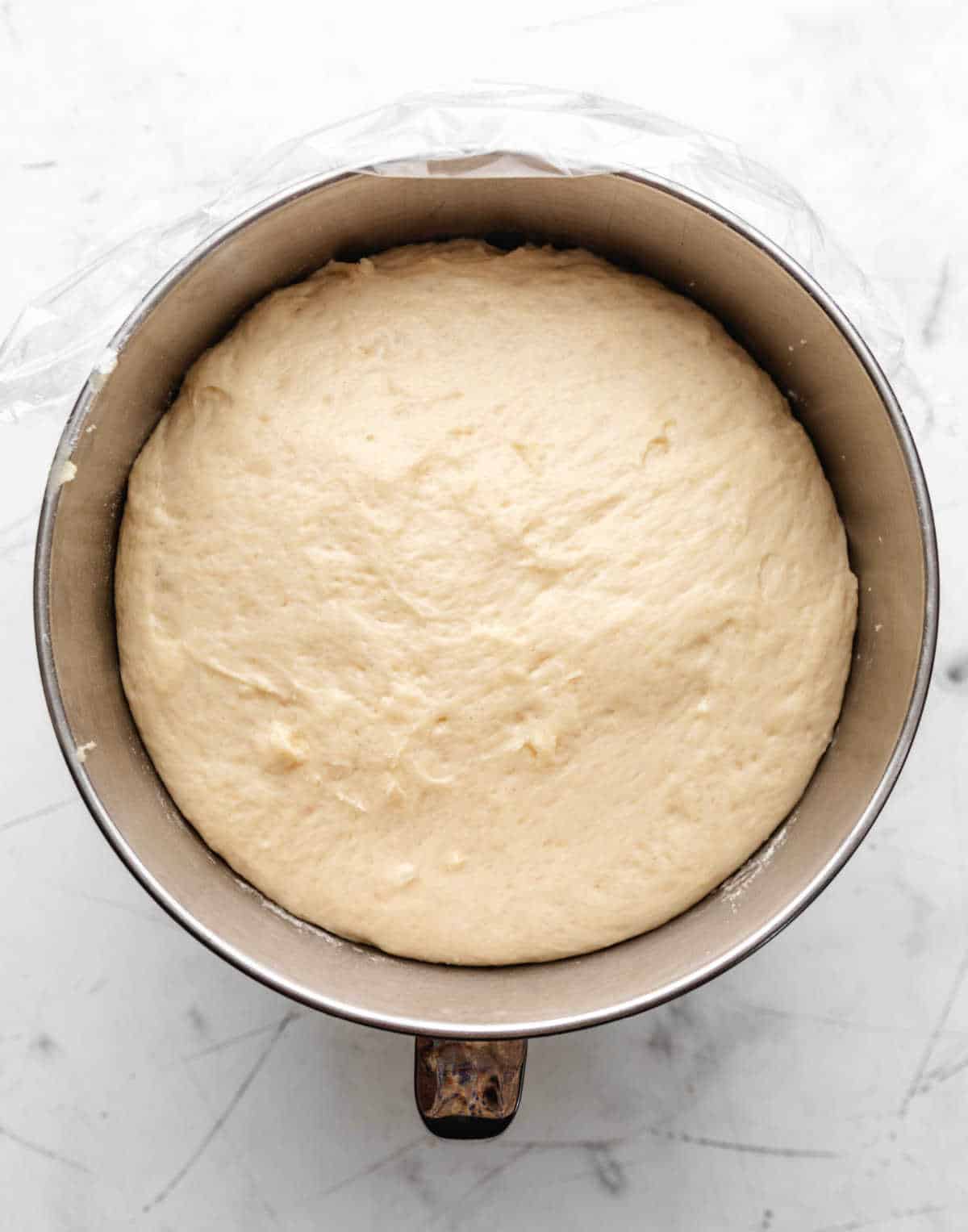 Risen potato roll dough in a silver mixing bowl. 