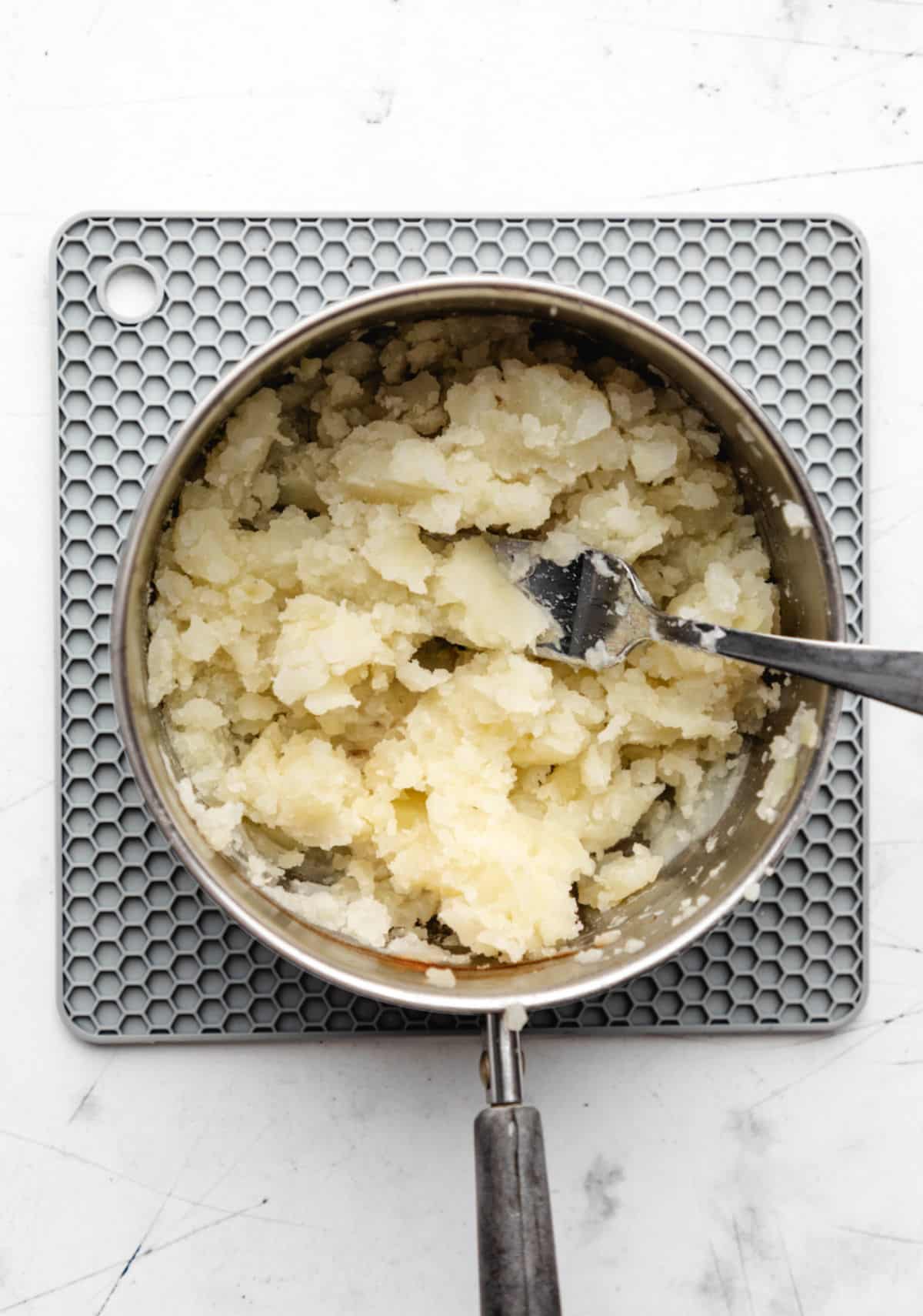 A fork mashing potatoes in a silver saucepan.