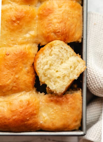 A pan of potato rolls with one roll on its side.