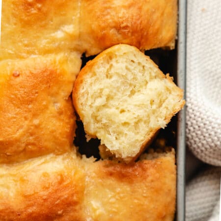 A pan of potato rolls with one roll on its side.