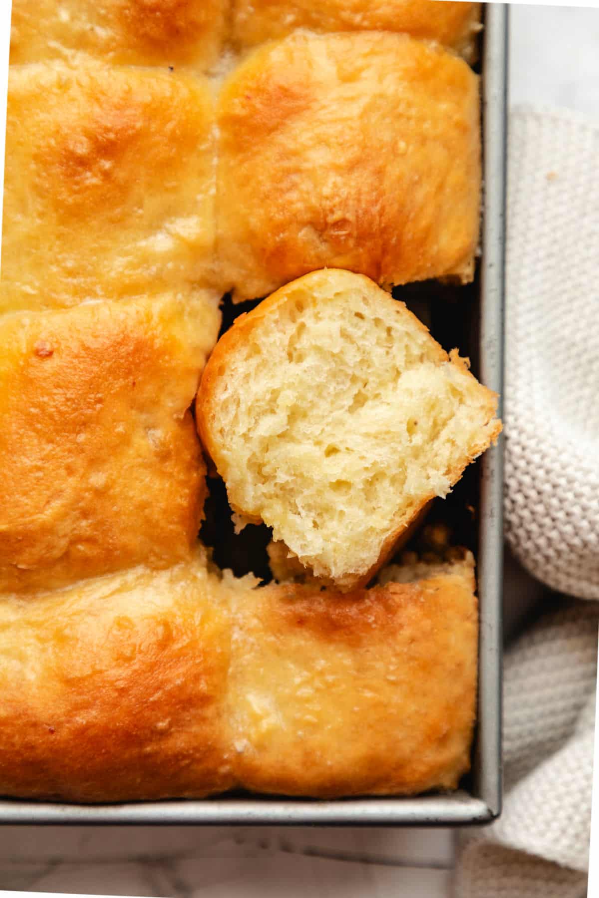 A pan of potato rolls with one roll on its side.