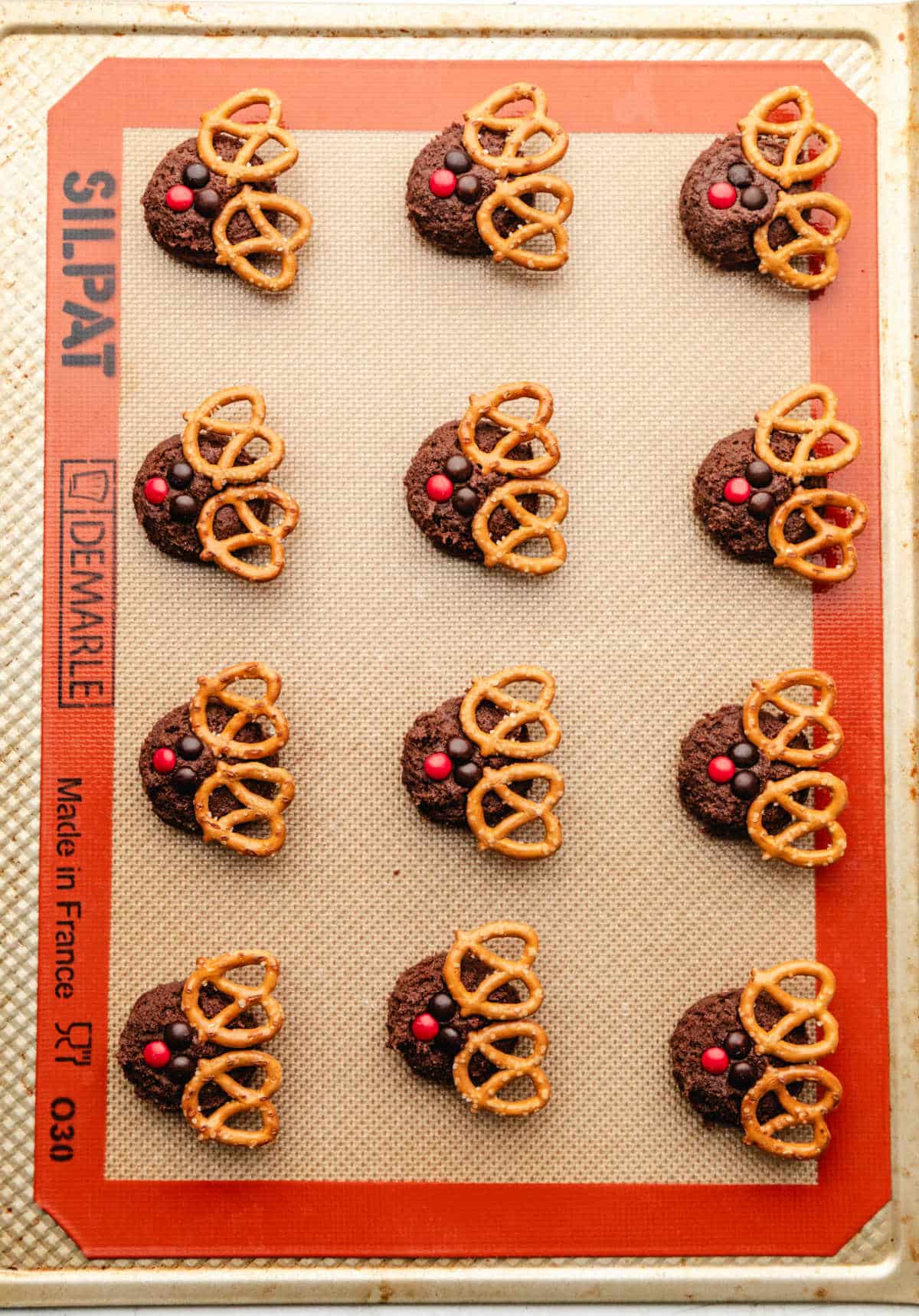 Rows of unbaked reindeer cookies on a silpat lined baking sheet.