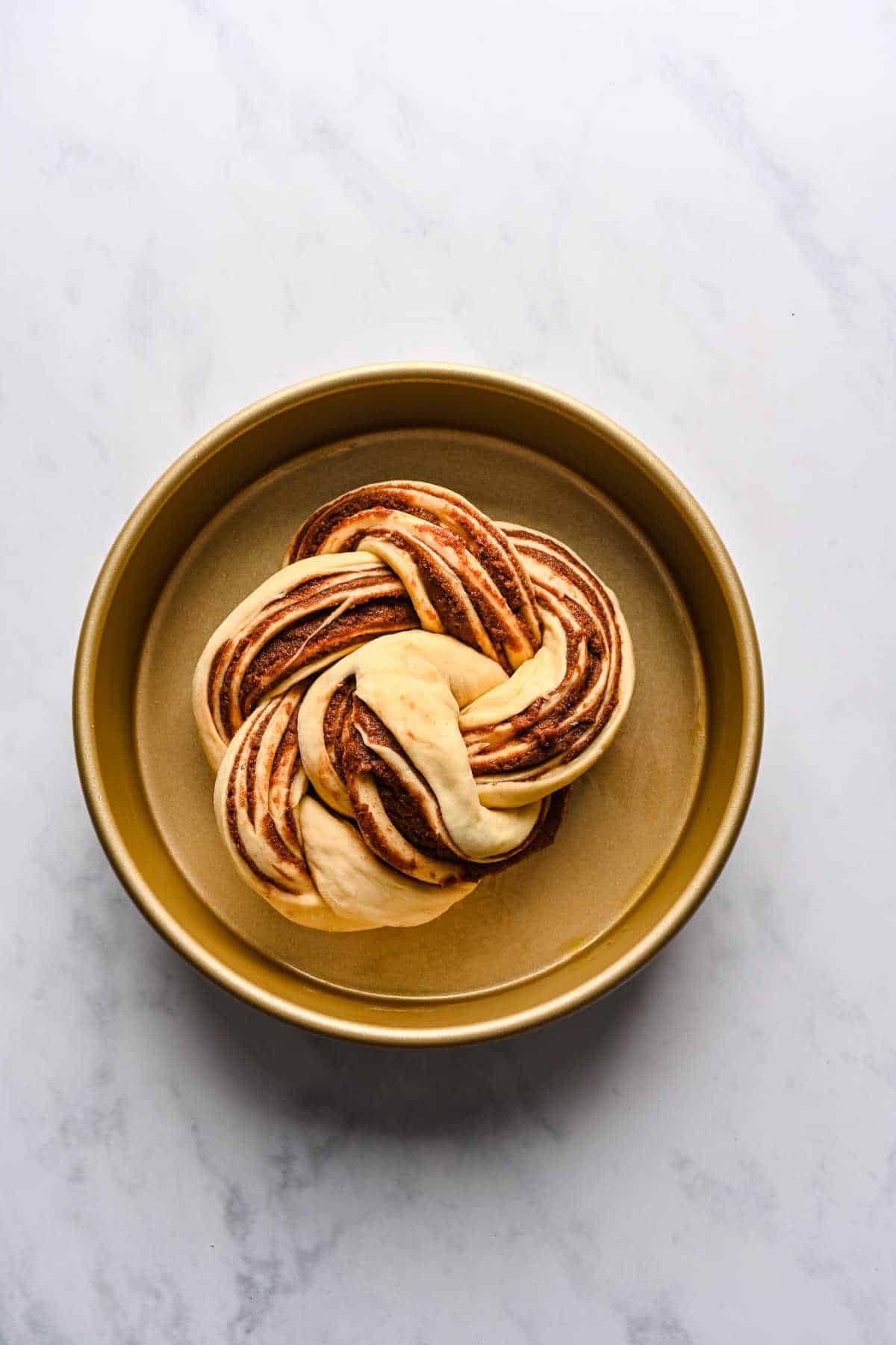 Braided cinnamon bread dough in a cake pan.