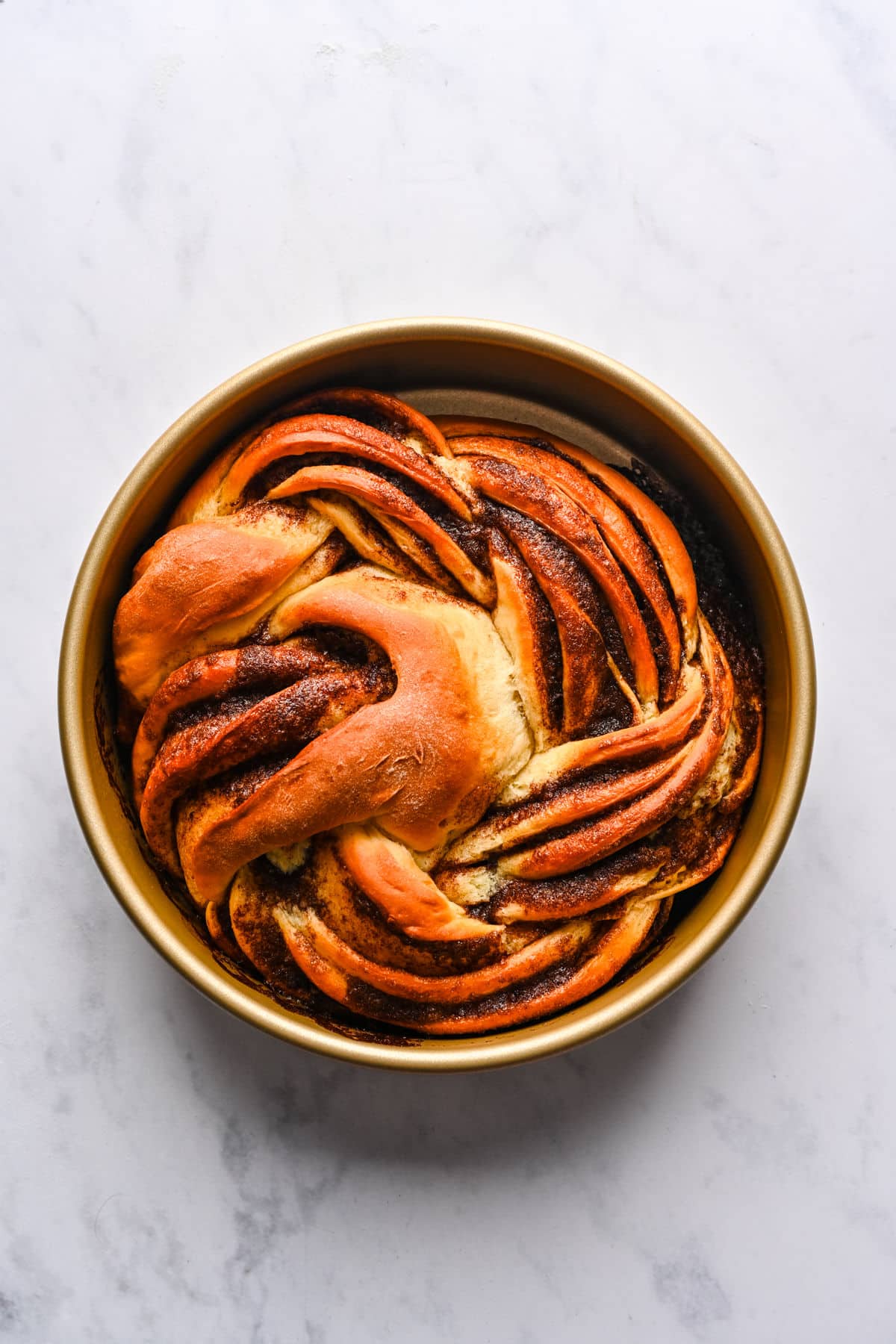 A baked loaf of braided cinnamon bread in a cake pan.