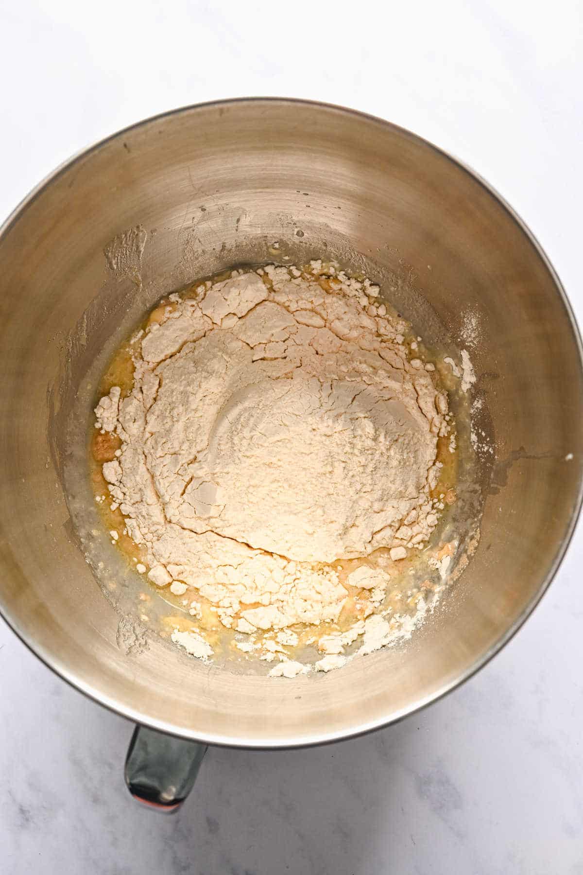 Flour on top of yeast and butter mixture in a silver mixing bowl. 