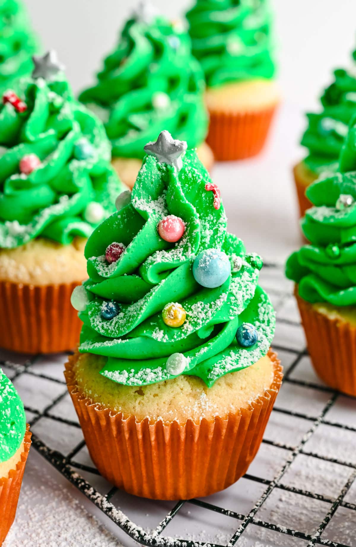 Christmas tree cupcakes dusted with powdered sugar on a wire cooling rack.