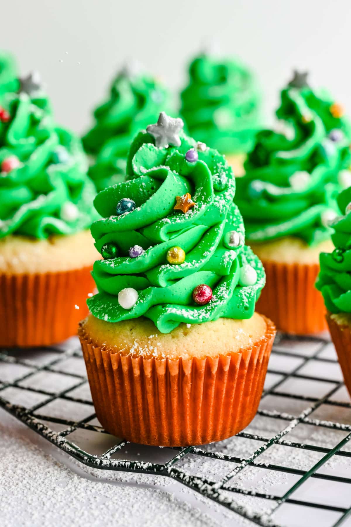 Rows of Christmas tree cupcakes on a wire baking rack.
