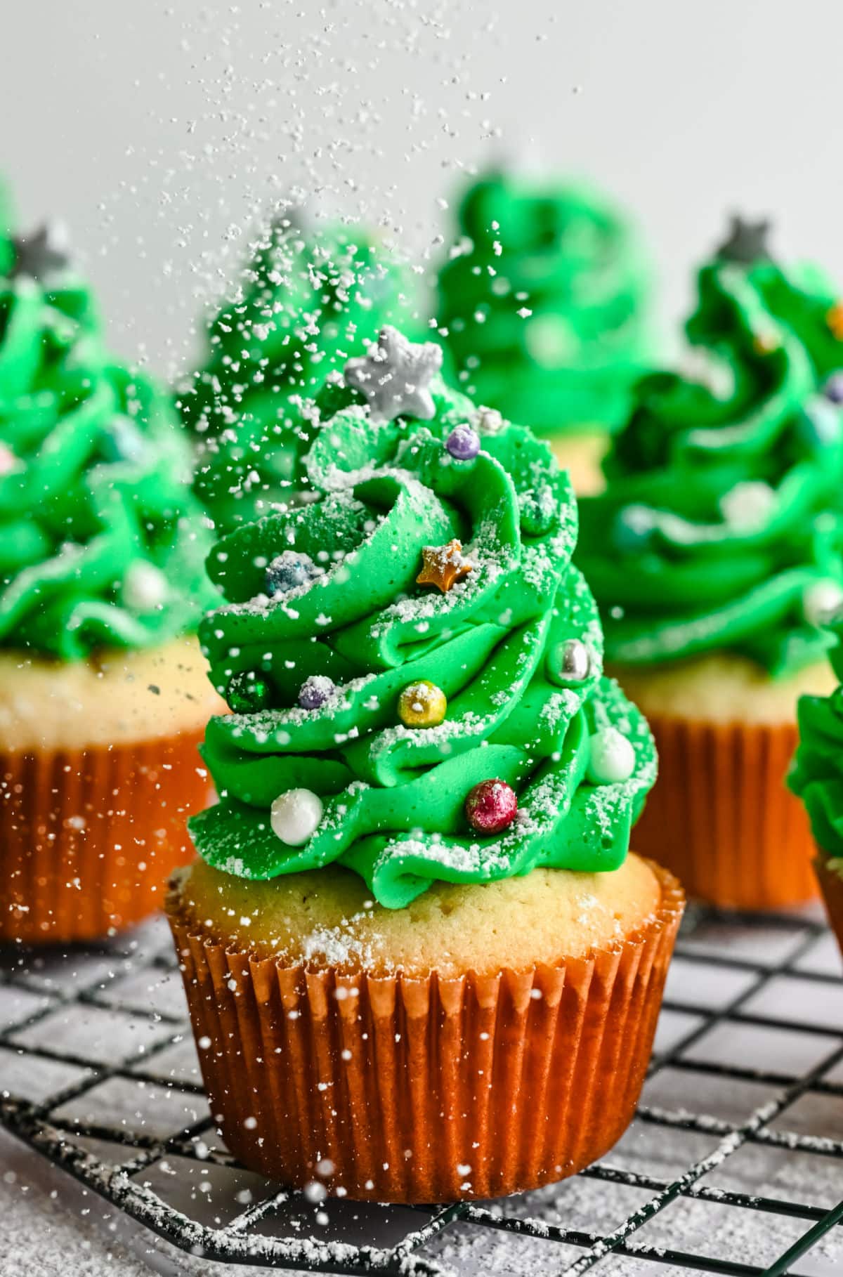 Powdered sugar sprinkling onto Christmas tree cupcakes.