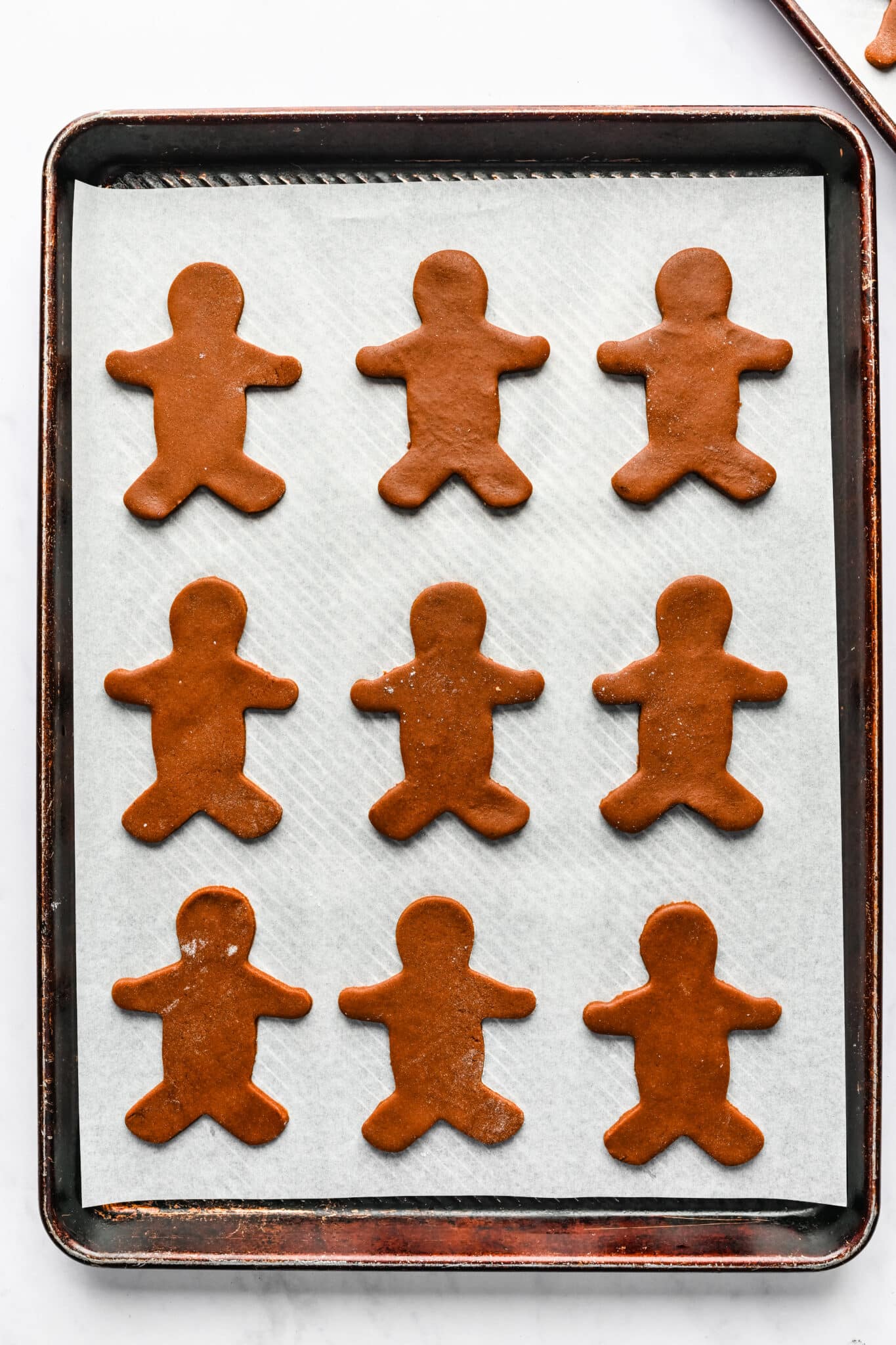 Gingerbread men cookie dough on a parchment lined baking sheet. 