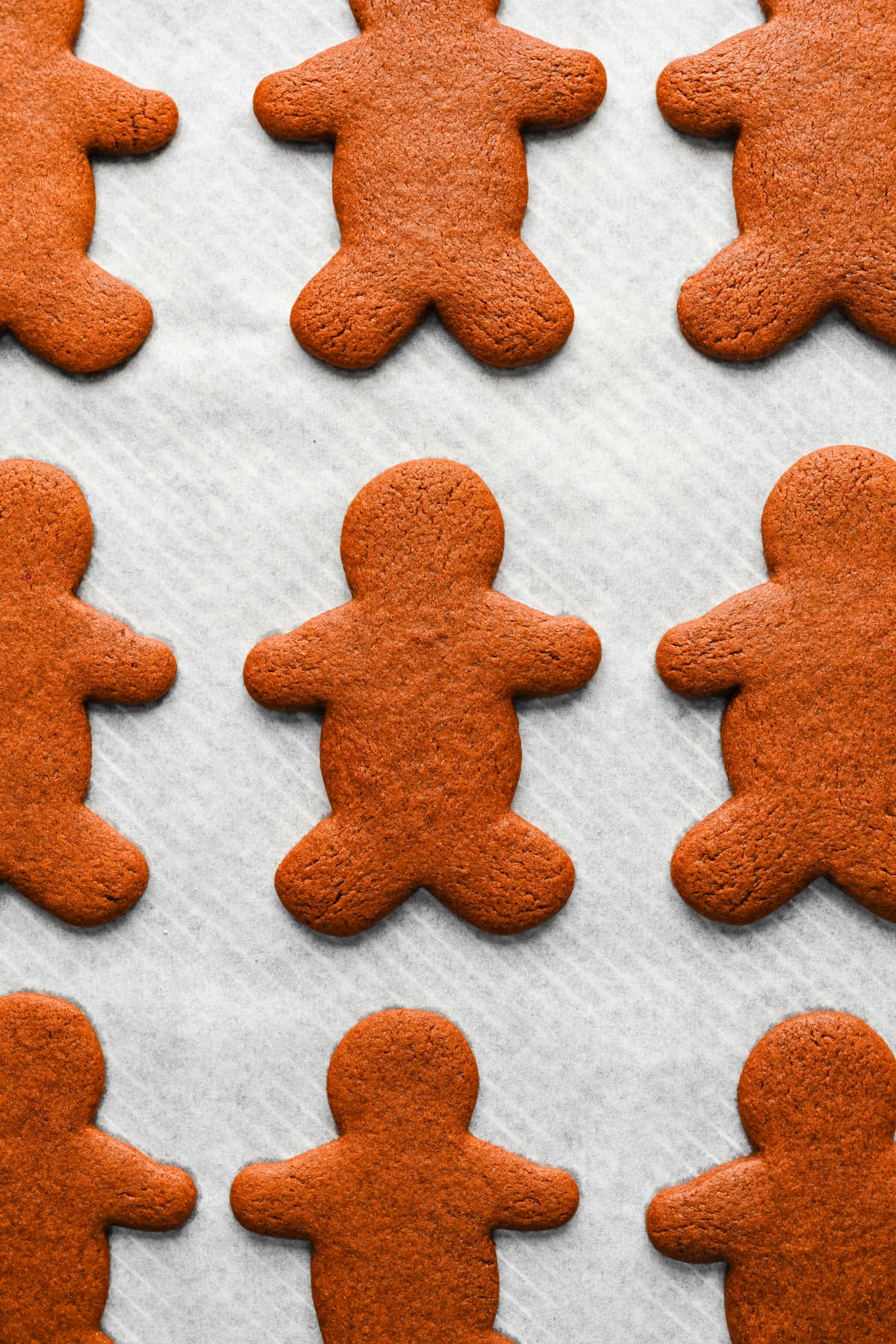 Baked gingerbread men cookies on a parchment lined baking sheet. 