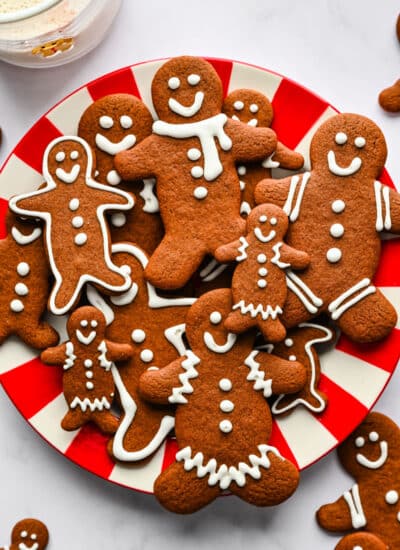 A red and white striped plate holding gingerbread men cookies stacked overlapping each other.