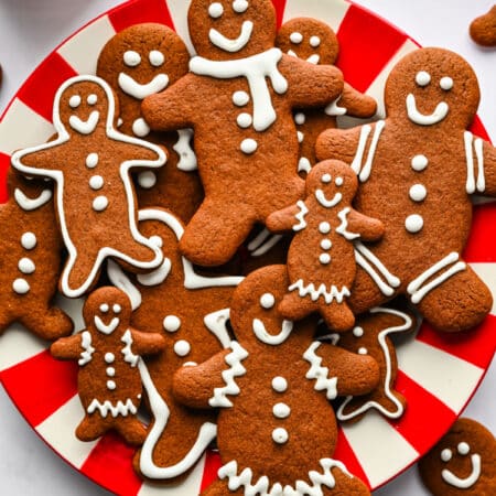 A red and white striped plate holding gingerbread men cookies stacked overlapping each other.