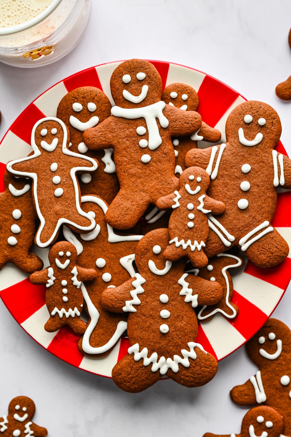 A red and white striped plate holding gingerbread men cookies stacked overlapping each other.