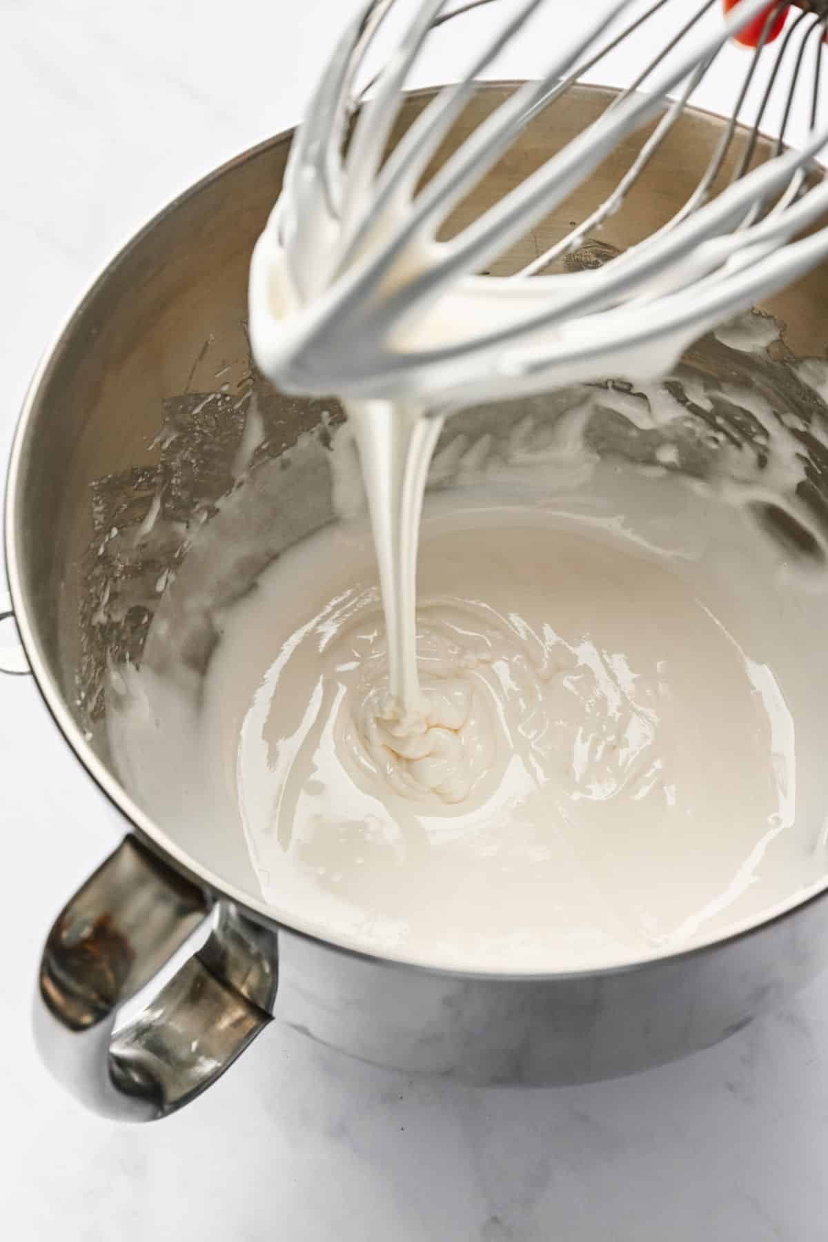 A wire whisk attachment with royal icing streaming off of it.
