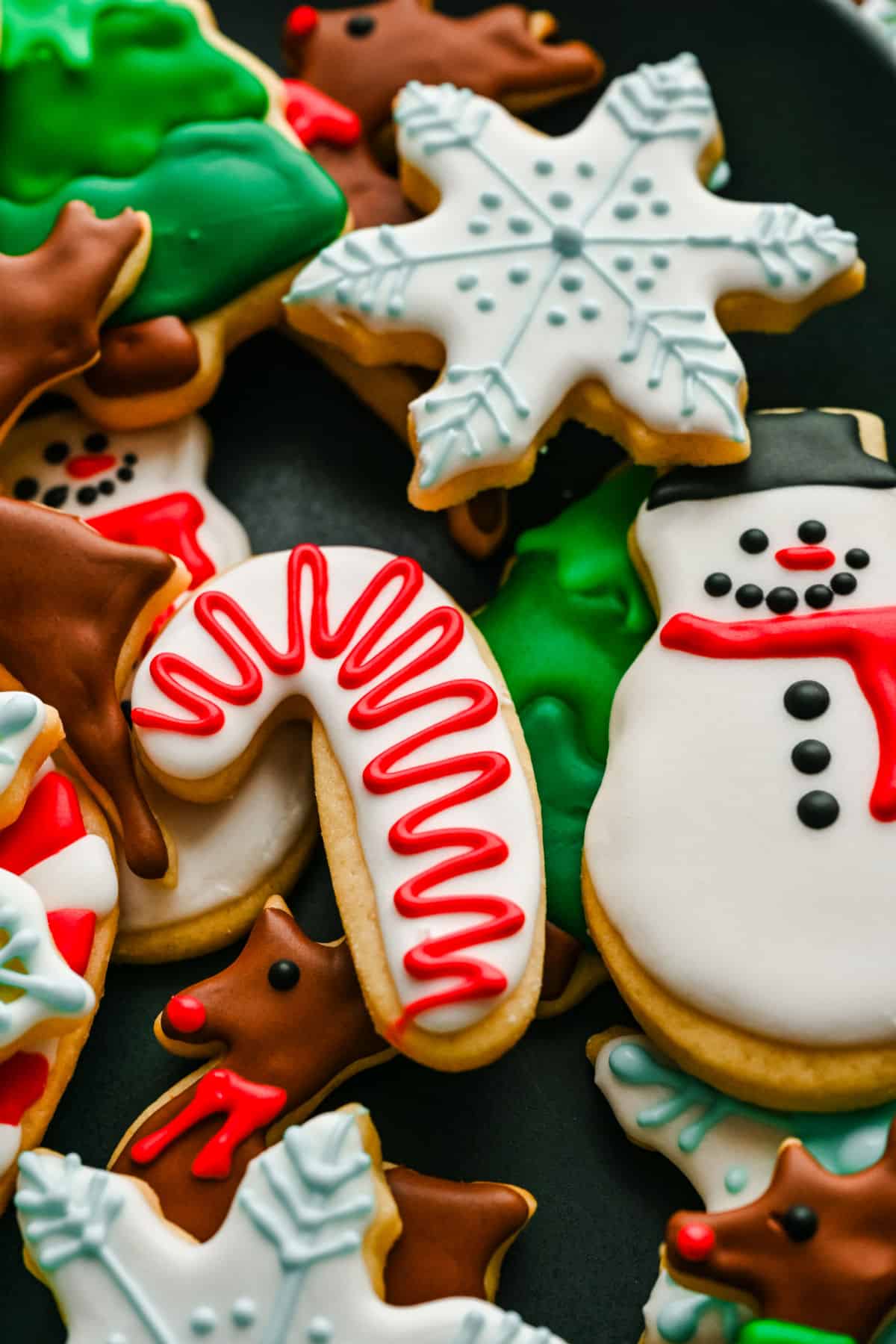 Candy cane and snowman cut out sugar cookies on top of decorated sugar cookies.