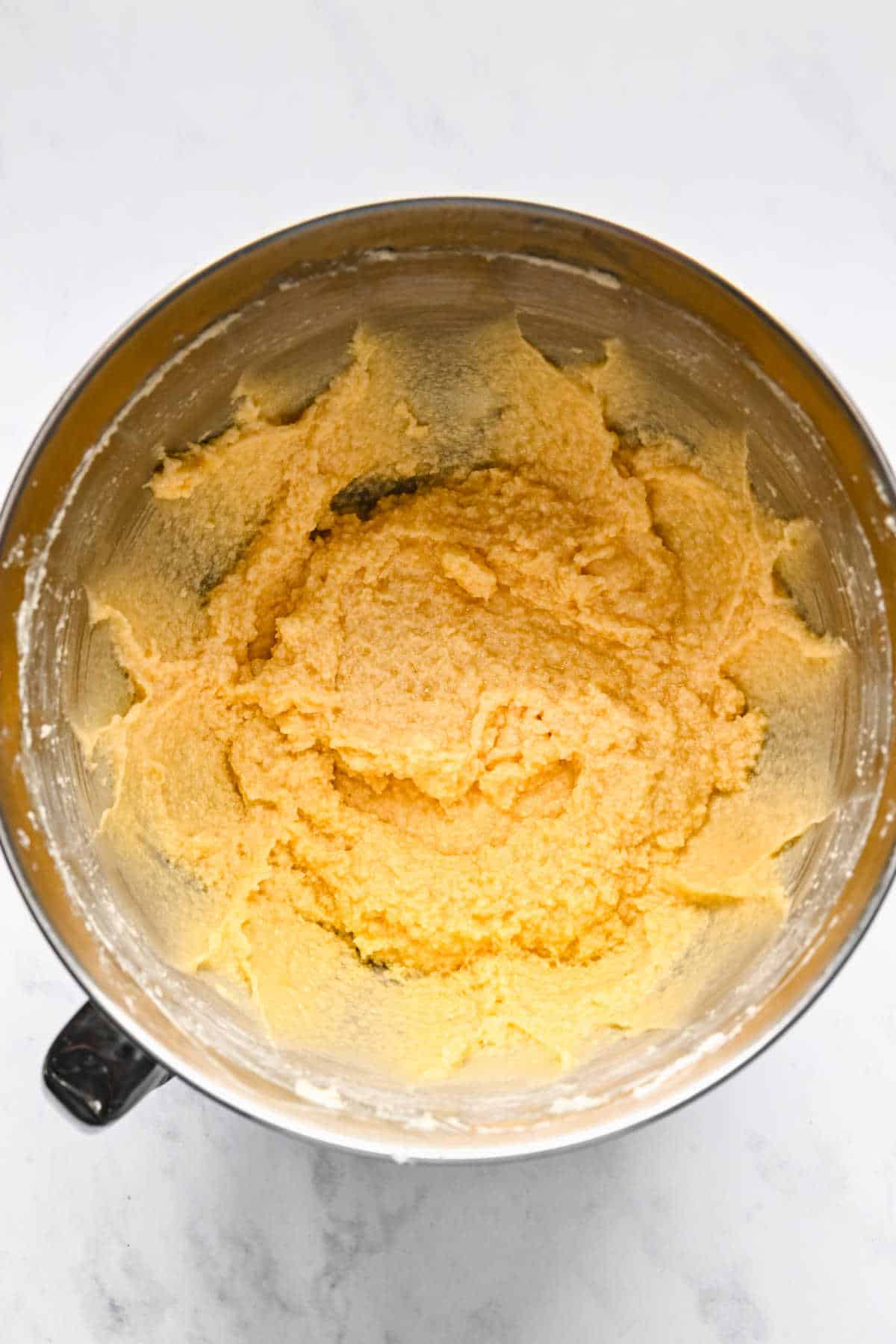 Eggs beaten into creamed butter mixture in a silver mixing bowl.
