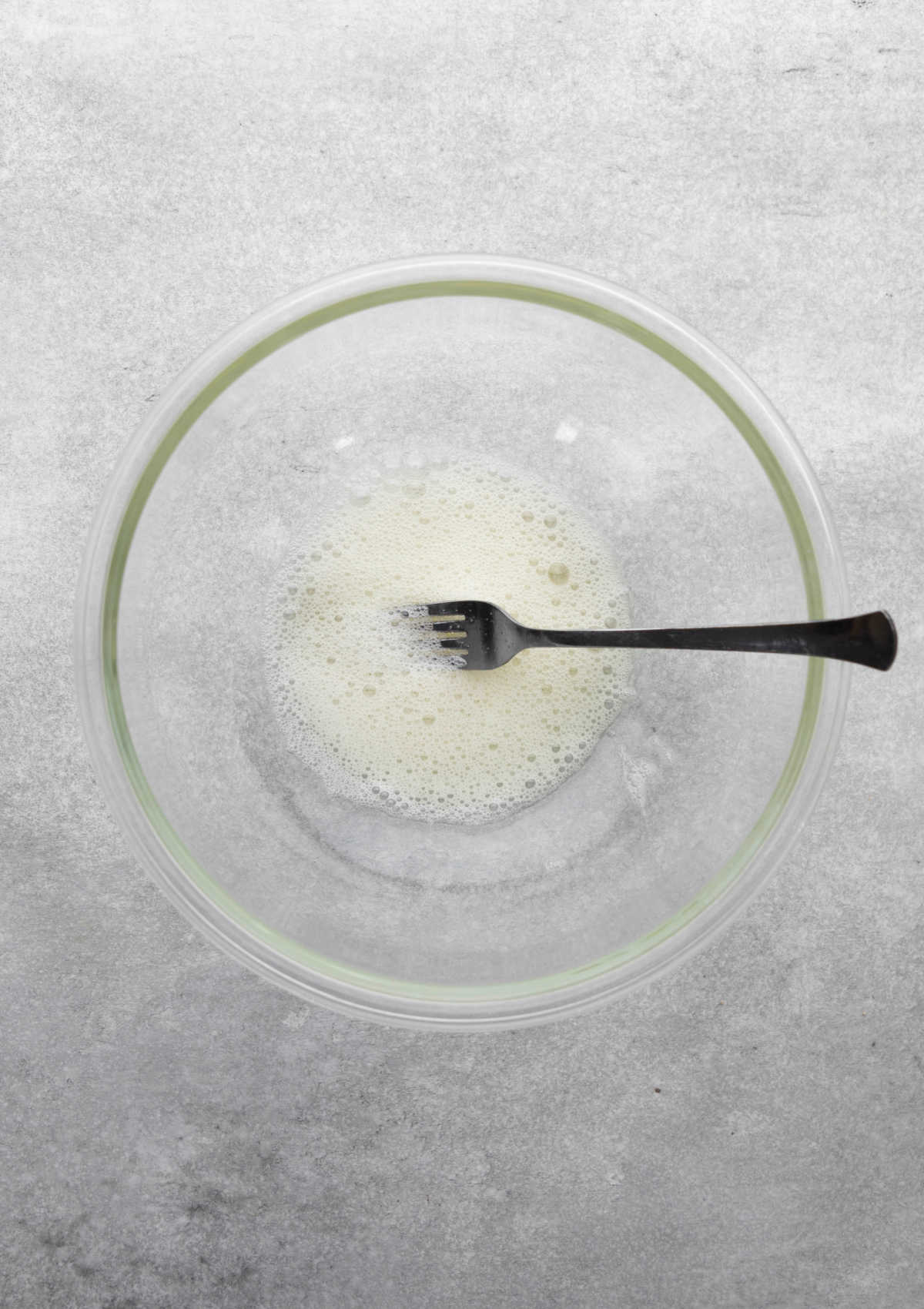 A frothy egg white in a glass mixing bowl. 