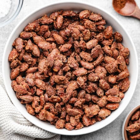 A white dish of candied almonds next to two spoons with cinnamon on them.