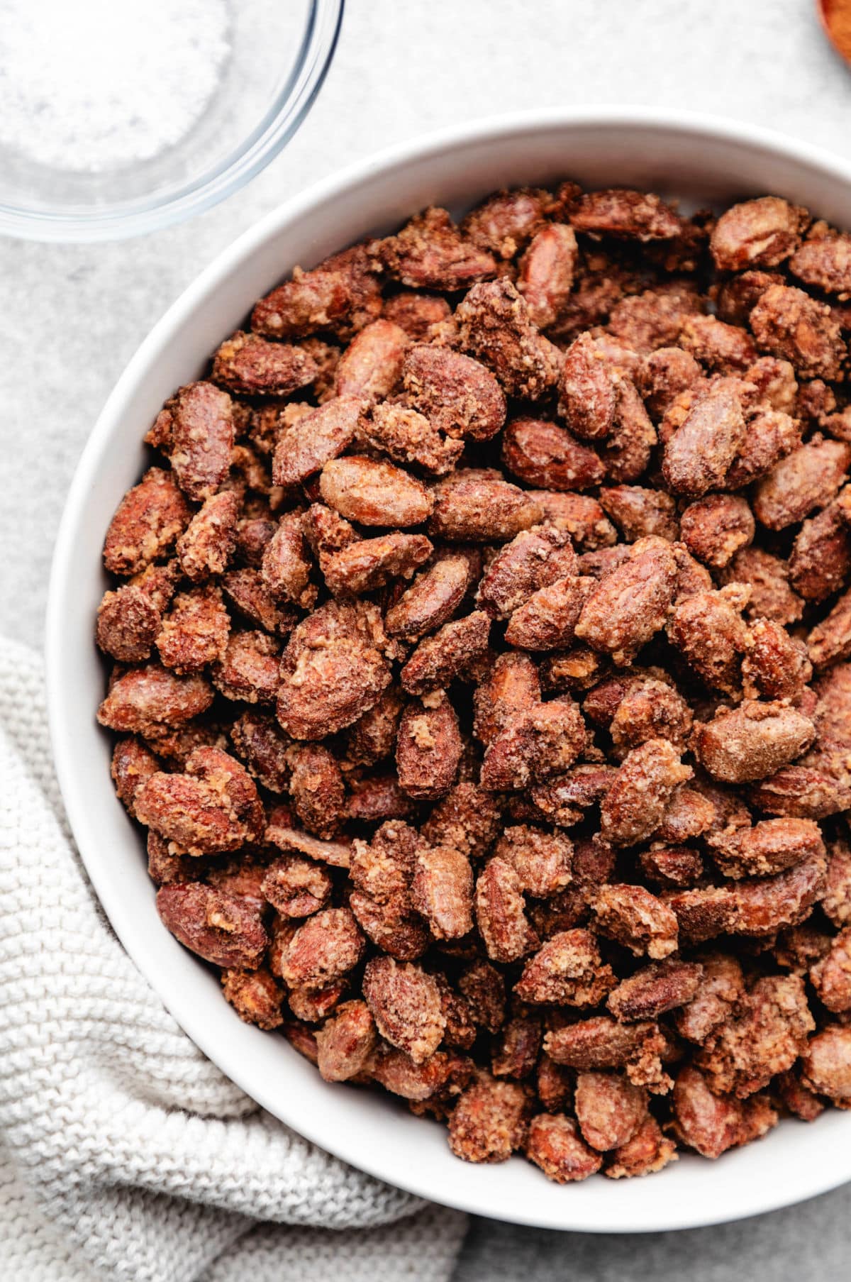 A white dish of candied almonds next to a dish of salt.