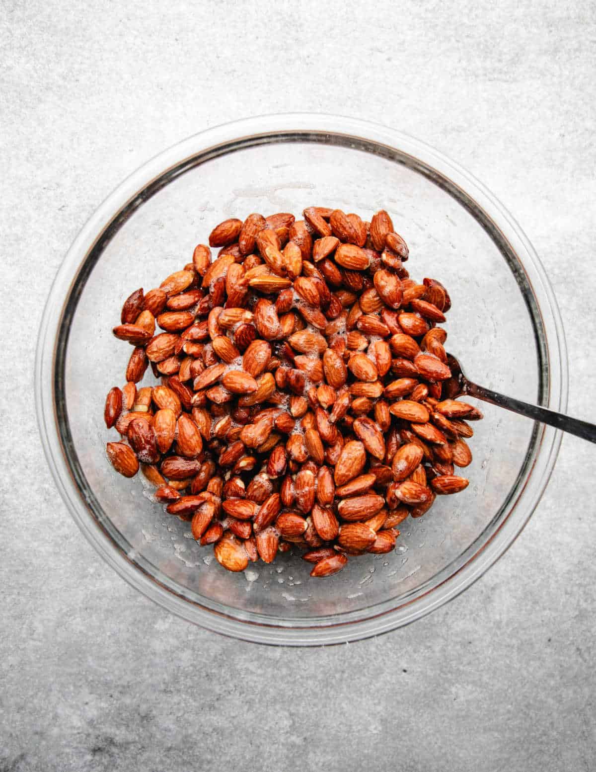 Almonds coated in egg mixture in a glass mixing bowl. 