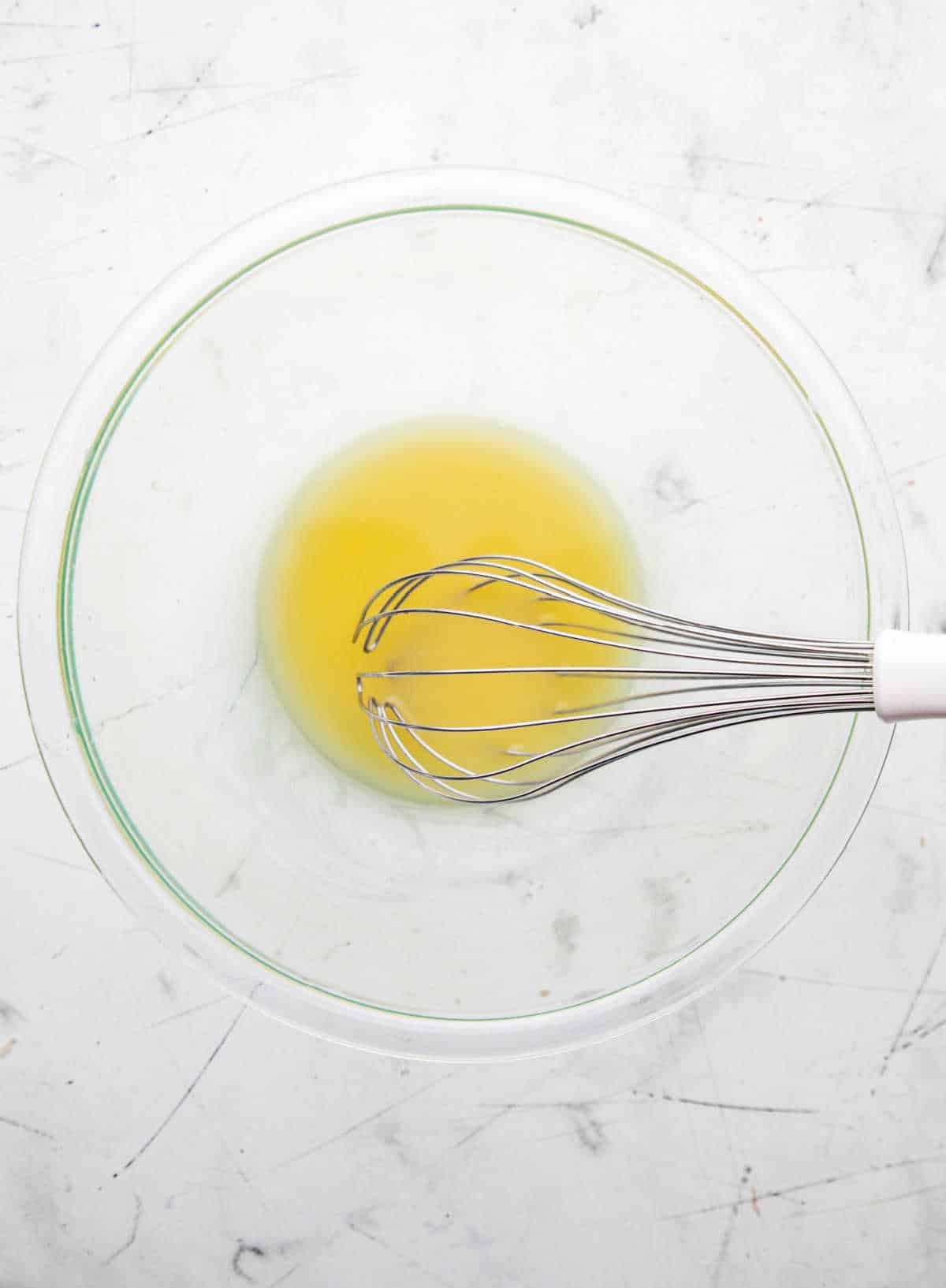 A whisk in a dish of melted butter. 