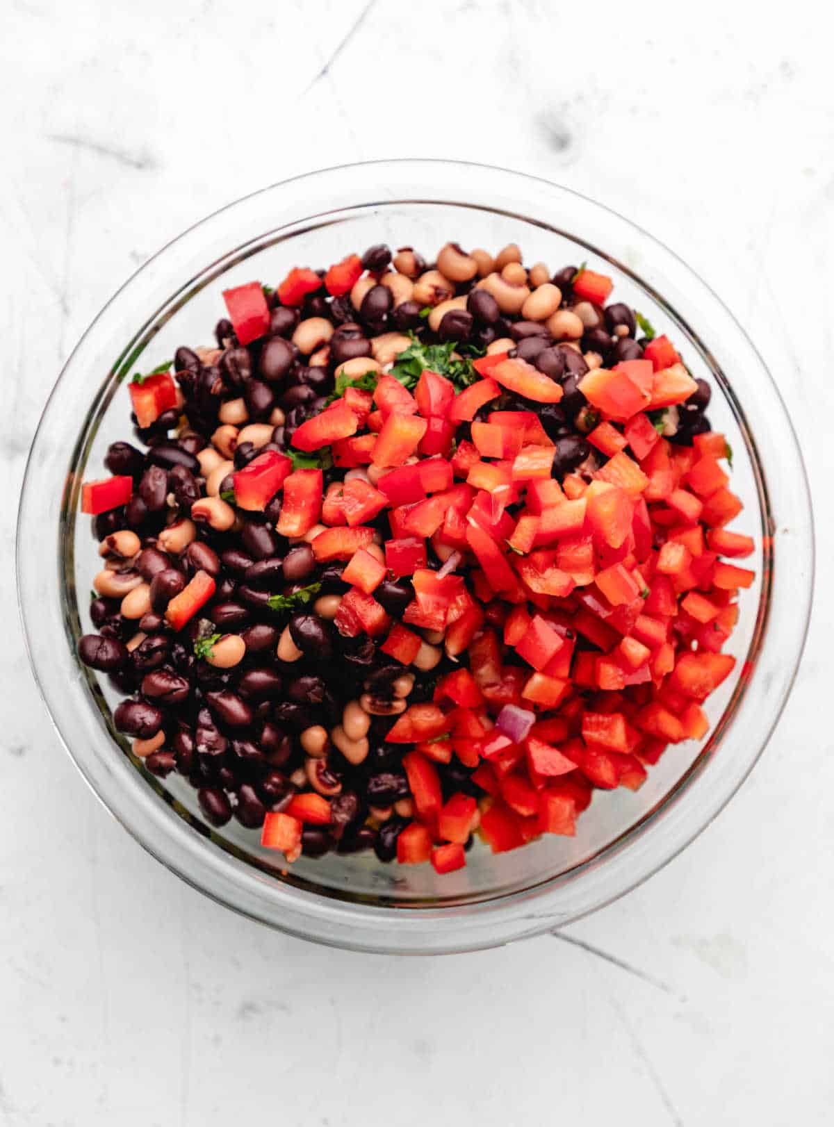 Veggies and beans for cowboy caviar in a glass mixing bowl. 