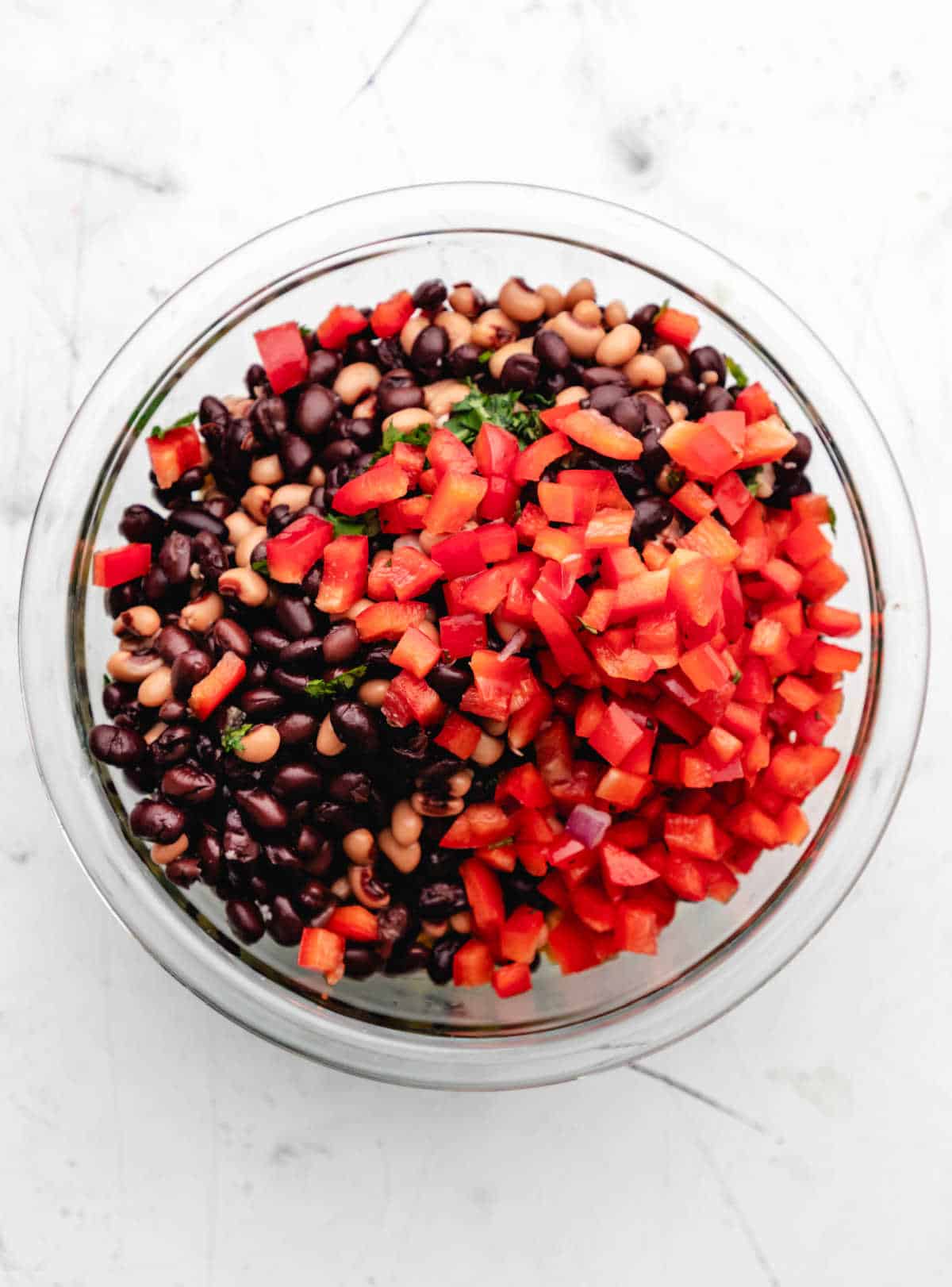 Veggies and beans for cowboy caviar in a glass mixing bowl.