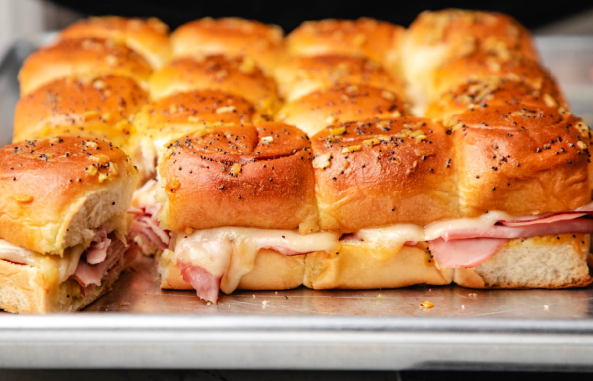 A row of  baked ham and  cheese sliders with one pulled away.