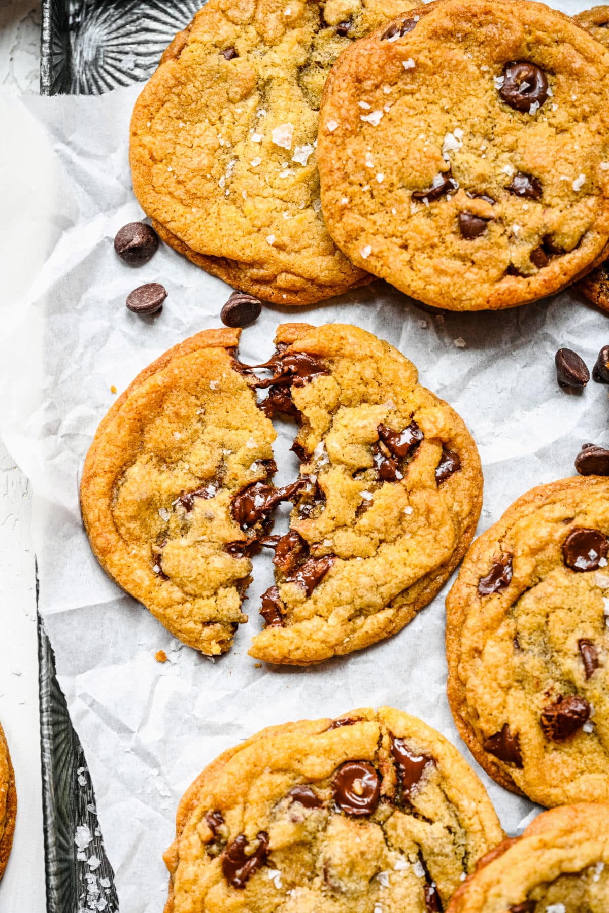 A chewy chocolate chip cookie broken in half on a piece of parchment paper. 