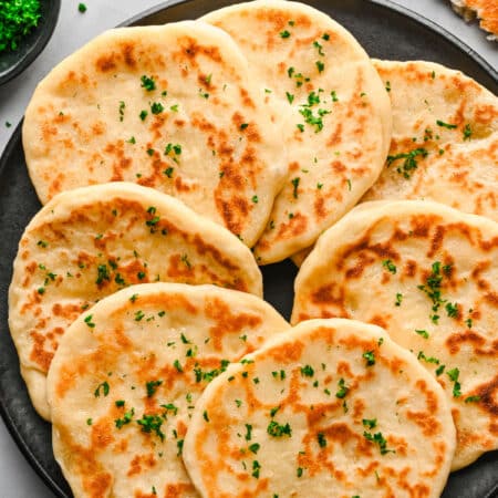 A plate of overlapping flatbreads topped with chopped parsley.