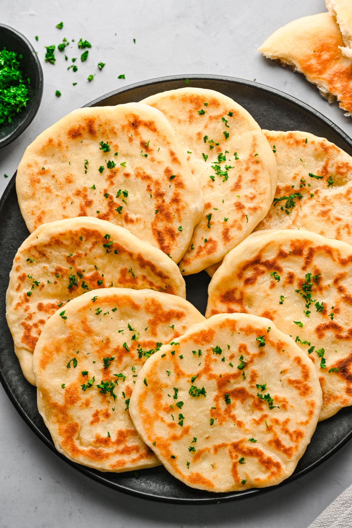 A plate of overlapping flatbreads topped with chopped parsley.