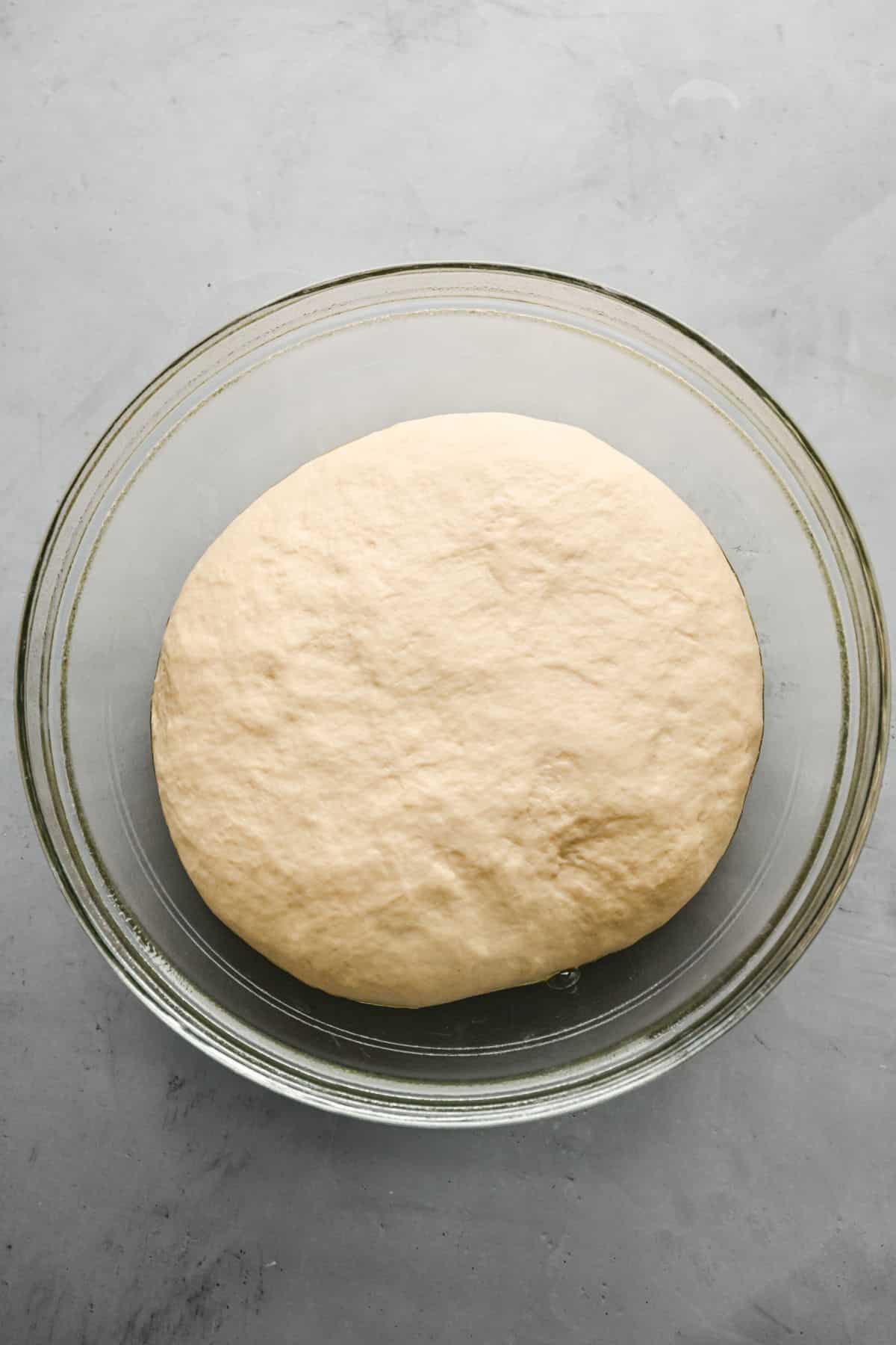 Risen flatbread dough in a glass mixing bowl. 